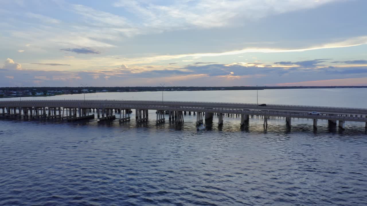 A series of cars glide over an elevated concrete bridge stretching across tranquil water, reflecting soft twilight hues that merge the geometry of engineering with the serenity of nature