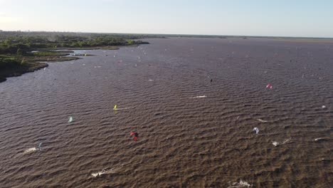 Aerial-flyover-wavy-river-with-many-Kitesurfer-surfing-on-stormy-water-during-sunny-day-in-Argentina