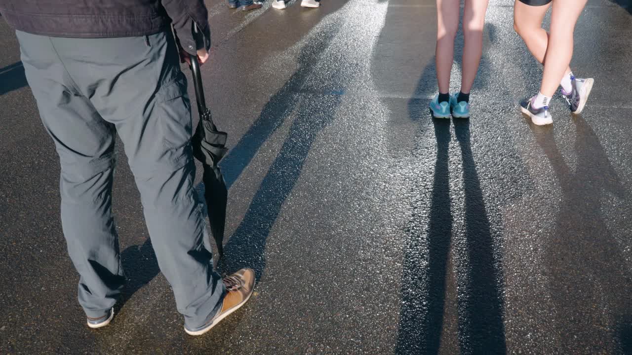 People Standing on a Wet Street with Their Shadows Cast on the Ground