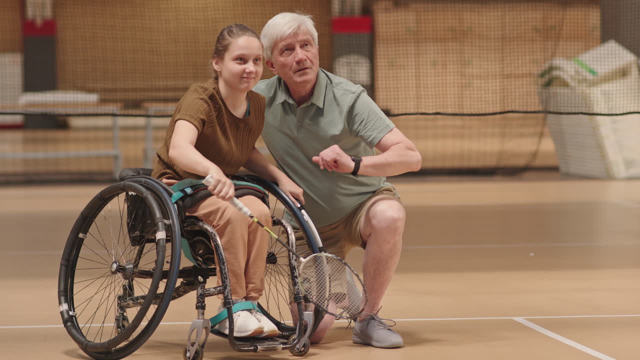 Coach Teaching Teenager in Wheelchair Play Badminton