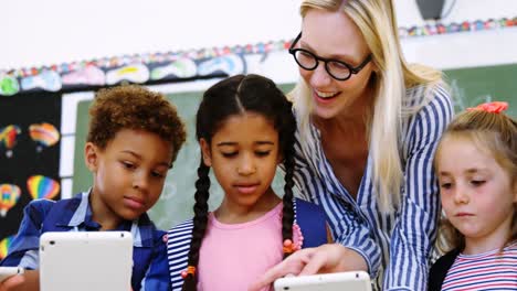 Teacher-assisting-schoolkid-on-digital-tablet-in-classroom