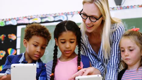 teacher assisting schoolkid on digital tablet in classroom