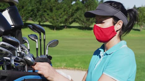 Mujer-Caucásica-Jugando-Al-Golf-Con-Máscaras-Faciales-Tomando-Un-Palo-De-Golf.