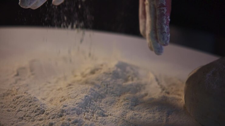 Primo piano di mani che setacciano la farina per l'impasto da forno