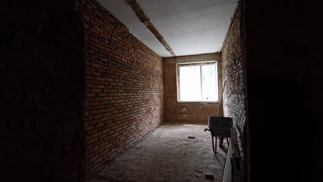 long room with brick walls and one window. wheelbarrow and a stick are at the wall. building renovation.