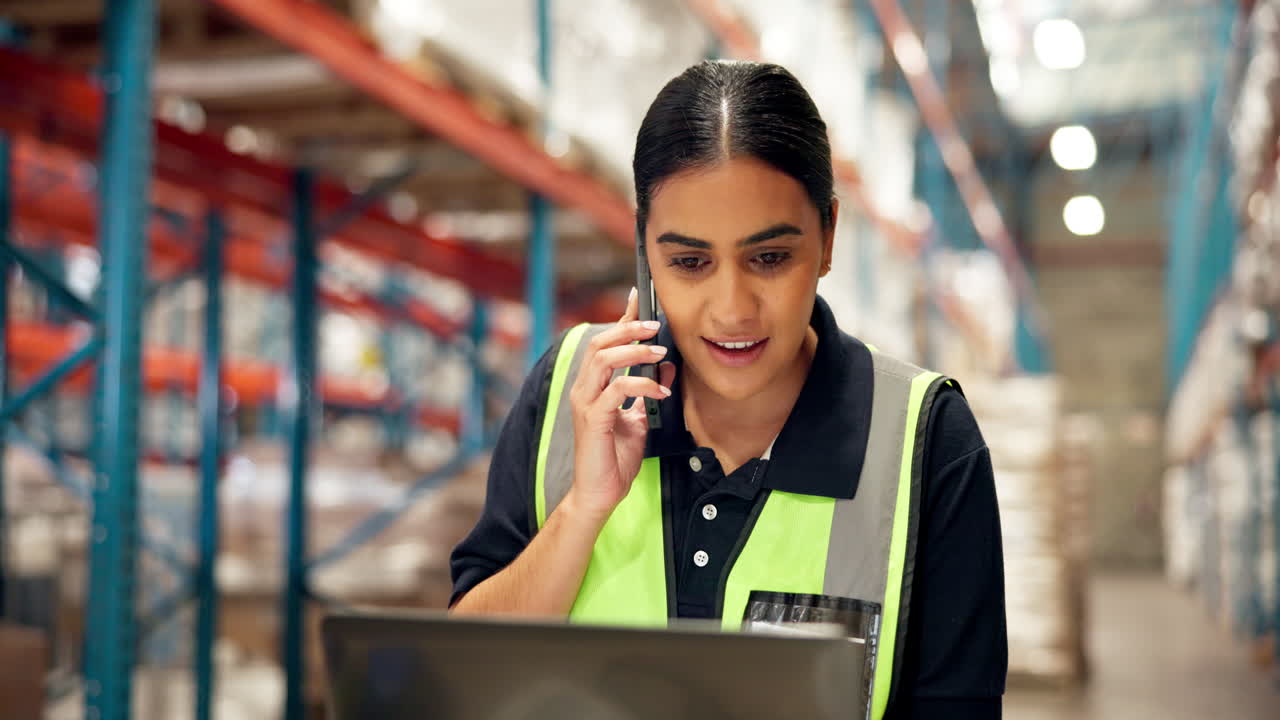 Employee in a warehouse taking a phone call while working on a laptop