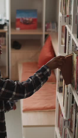 dark-skinned guy scans shelf for book. african american student makes selections for individual task in university library. man explores offerings in bookstore