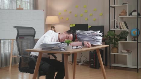 hombre asiático cansado durmiendo debido a trabajar duro con documentos en la oficina
