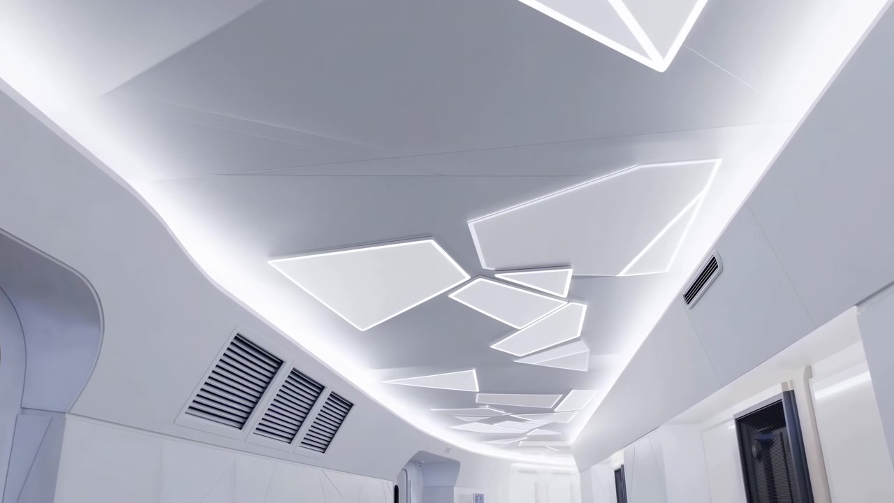 Vista dal basso del soffitto di un corridoio bianco con pannelli LED incassati pentagonali e trapezoidali sfalsati che brillano uniformemente, creando forte profondità, simmetria e un sottile flusso in avanti attraverso un ambiente moderno.