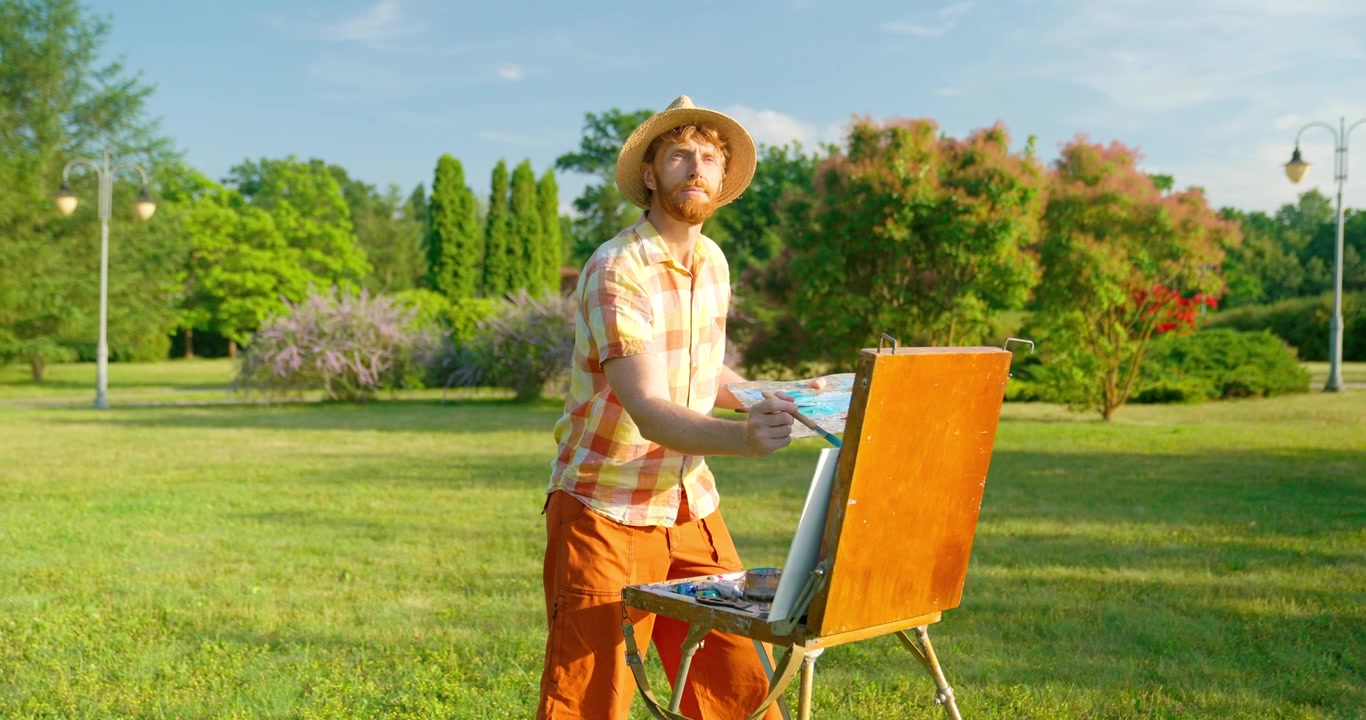 Artista uomo che dipinge su un cavalletto in un parco verde