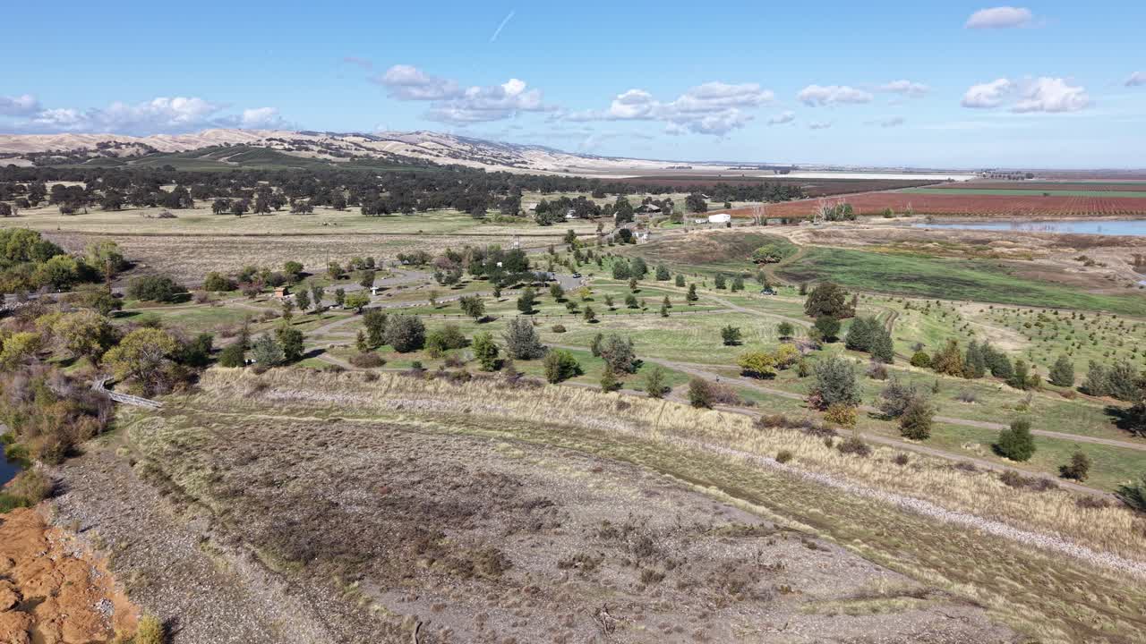 Drone footage moving laterally from left to right over Capay Valley in California, showing Cache Creek, dry vegetation, farmlands, and distant hills under a clear sky