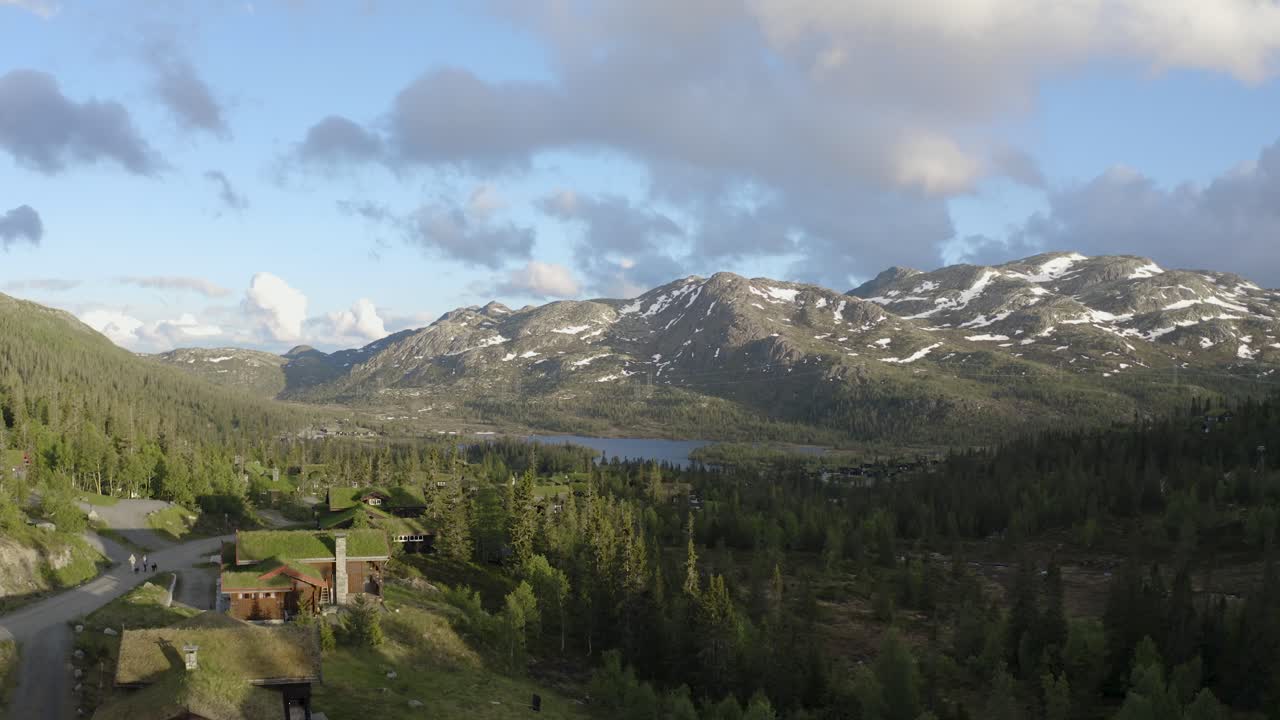Drone ascends slowly over cabins towards lake in mountain landscape Norway 4K