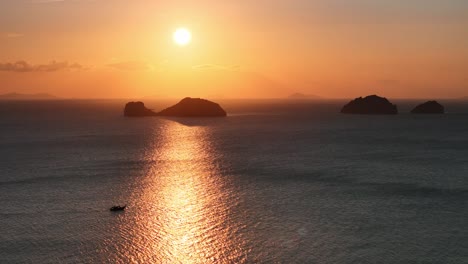 sun going down at the sea, shining a boat among the islands in a distance