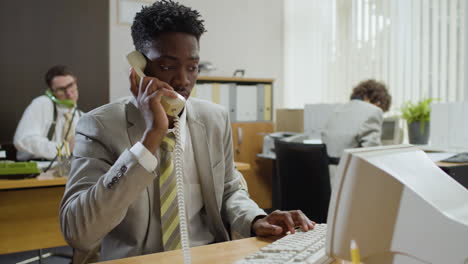Afroamerikanischer-Geschäftsmann,-Der-Am-Schreibtisch-Sitzt-Und-In-Einem-Vintage-Büro-Telefoniert.