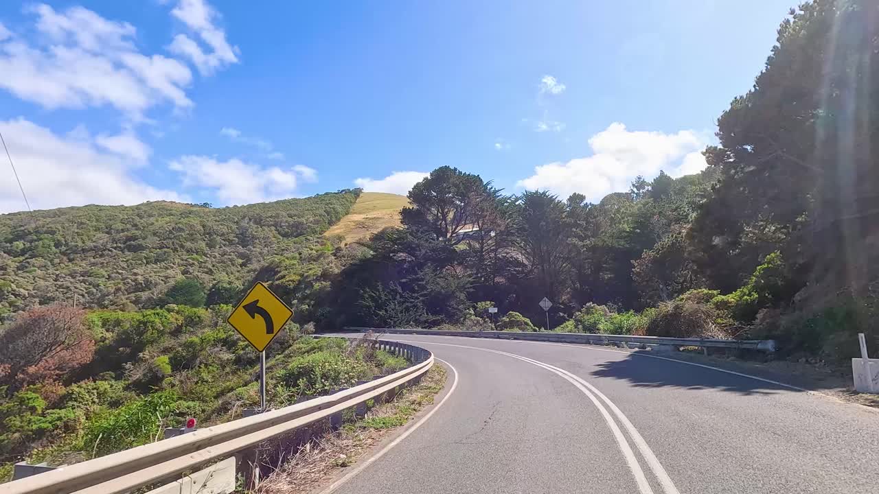 A 14-second video captures a serene drive along the winding Great Ocean Road, showcasing lush greenery and clear blue skies