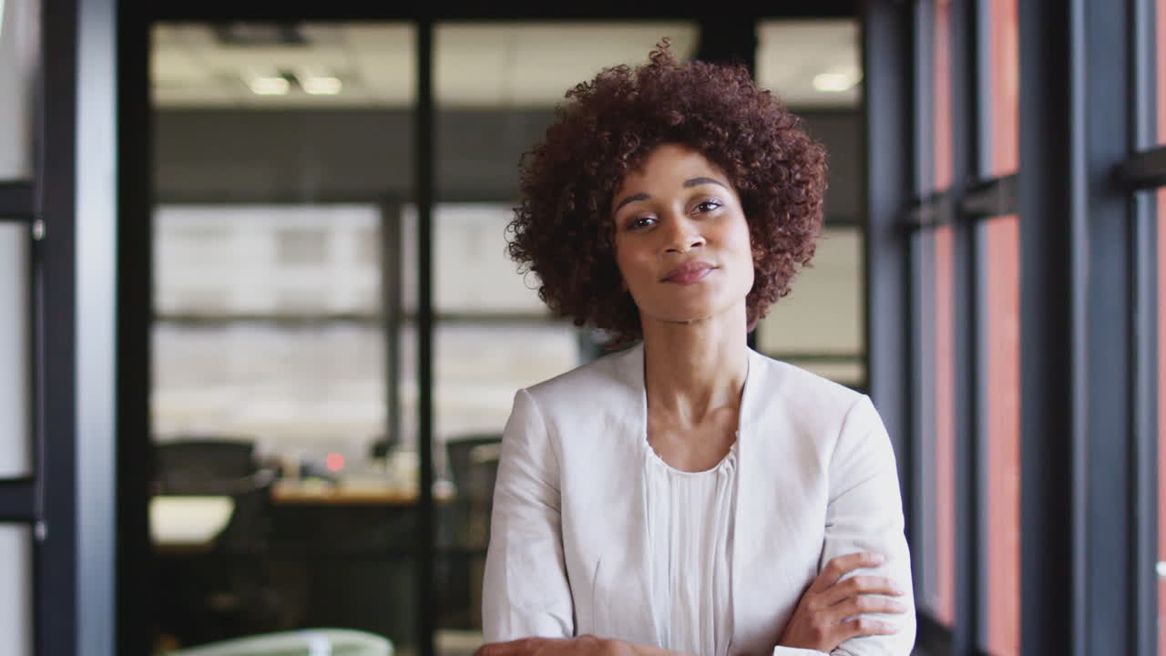 mujer de negocios negra del milenio sonriendo a la cámara por la ventana en una oficina, de cerca