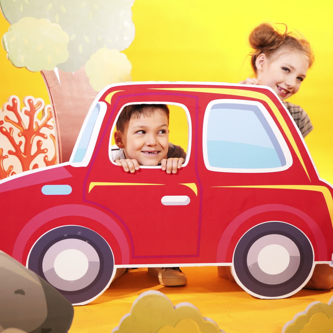 Bambini felici con una grande macchina giocattolo su uno sfondo di parete giallo brillante. Scenografia per bambini in studio