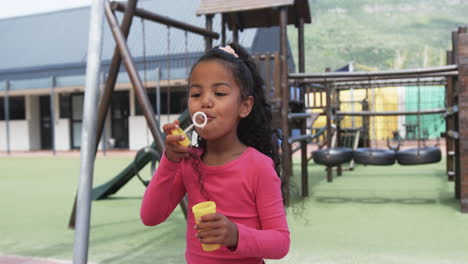 in a school playground, a young biracial girl is blowing bubbles