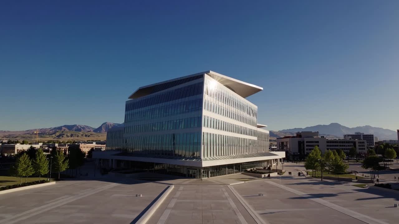 Modern architectural structure with sleek glass facade and angular roof design, showcasing dynamic angles and reflections in a vibrant urban setting with clear blue skies