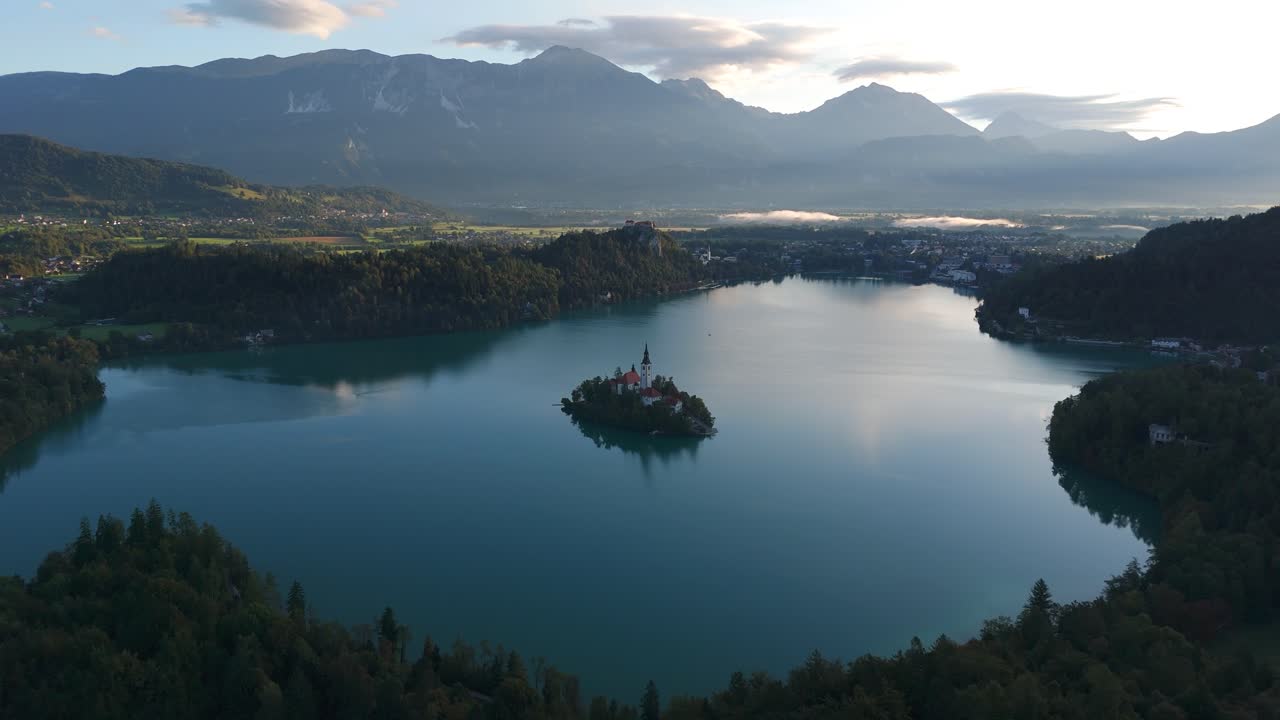 Il lago di Bled circonda la sua minuscola chiesa sull'isola, ai piedi delle vette alpine, con un fluido volo in drone in avanti
