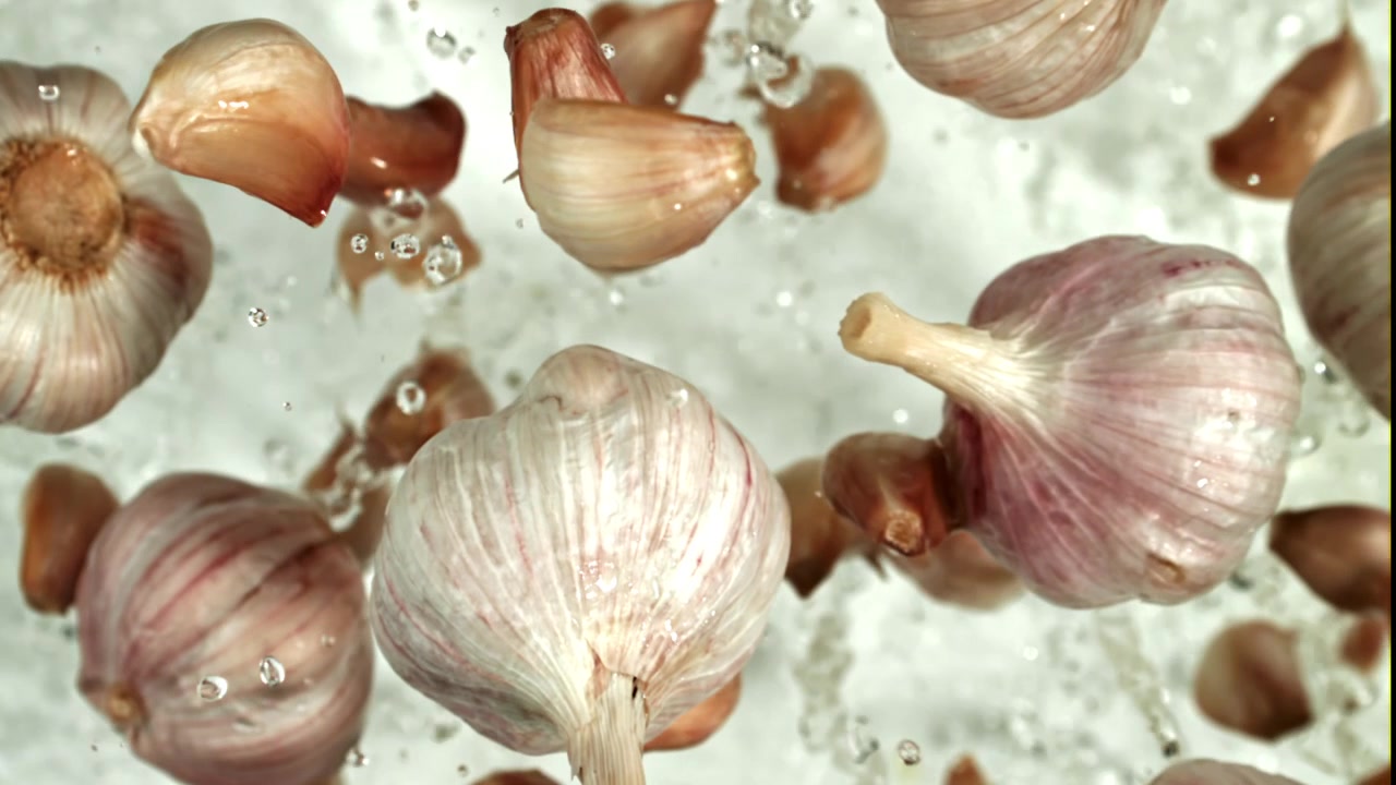 Bulbi e spicchi d'aglio freschi che schizzano nell'acqua.