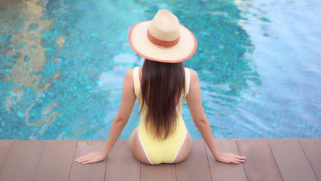 Una-Joven-En-Forma-Se-Sienta-De-Espaldas-A-La-Cámara,-Con-Vistas-Al-Agua-En-Una-Piscina