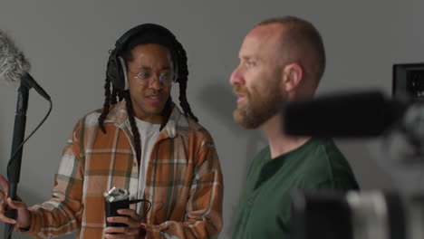 two men are in a recording studio, one is holding a microphone and the other is listening