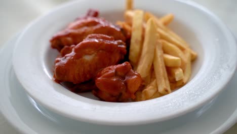 Alas-De-Pollo-De-Búfalo-Con-Papas-Fritas-Servidas-En-Un-Plato-Blanco