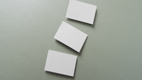 overhead view of three white business cards arranged on grey background, copy space, slow motion