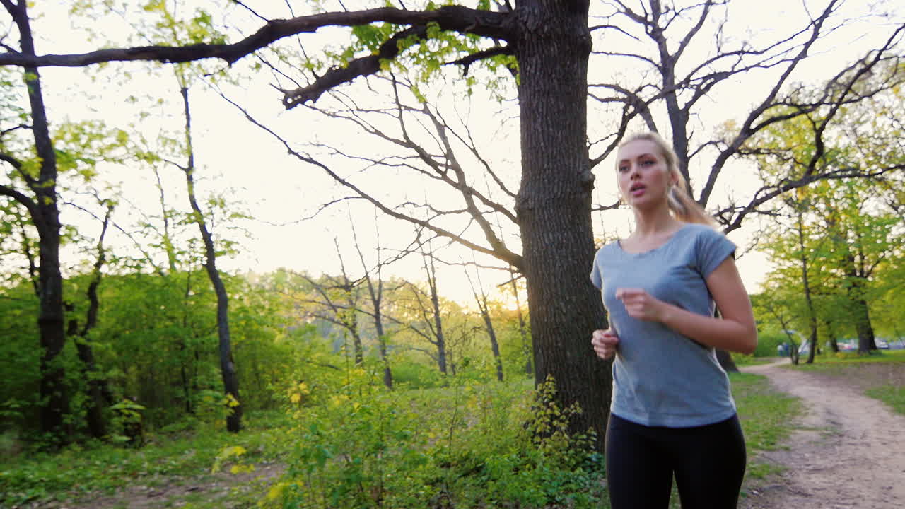 hermosa mujer en camiseta hace una carrera en el tiro de steadicam del bosque de primavera