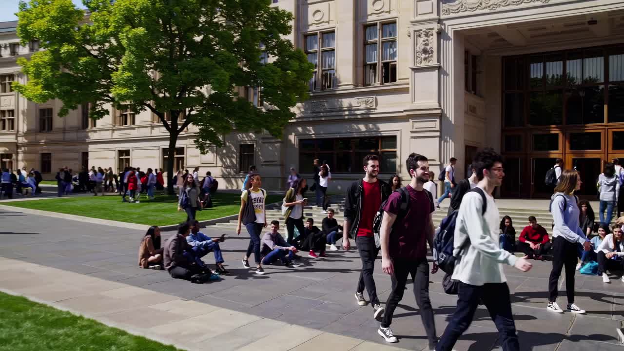 A lively campus scene video captures students walking and sitting outside a historic building, shot