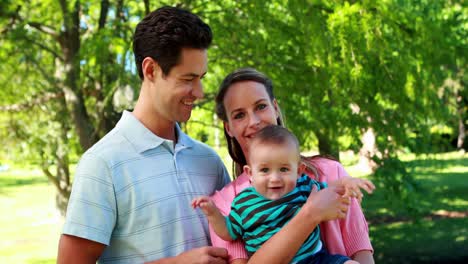 Young-couple-holding-their-baby-son-smiling-at-camera-in-the-park
