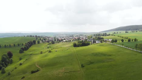 Aerial-of-small-rural-village-in-Germany-on-green-hills-in-summer