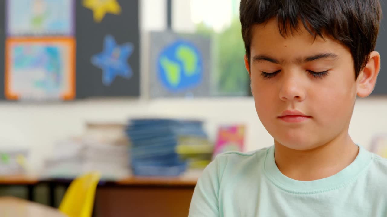 vista frontal de un escolar caucásico sentado en el escritorio en el aula de la escuela 4k