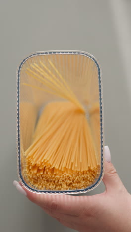 woman puts spaghetti into transparent plastic container and closes lid shaking upper view. young lady packs raw food into convenient box for storage