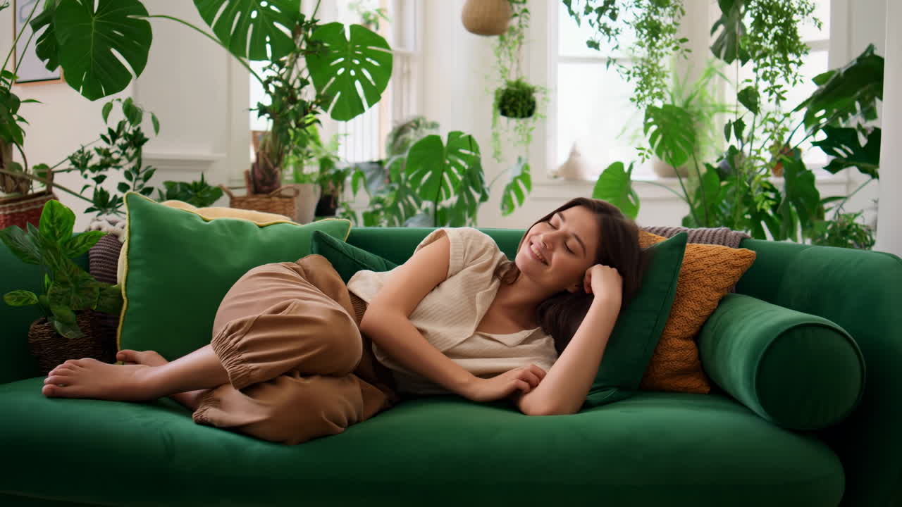 Jovem Mulher Relaxando em um Sofá Verde Rodeada por Plantas de Interior