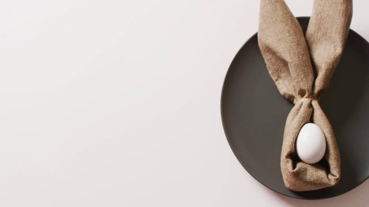 Egg and ribbon in shape of rabbit on plate on white background with copy space