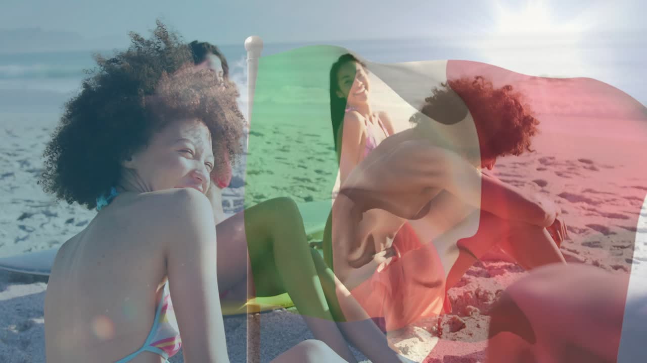 Friends sitting on beach, wind sweeping flag across faces, laughing while socializing for lifestyle