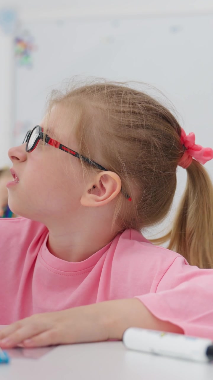 Primo piano di una bambina con gli occhiali che cancella a una scrivania.