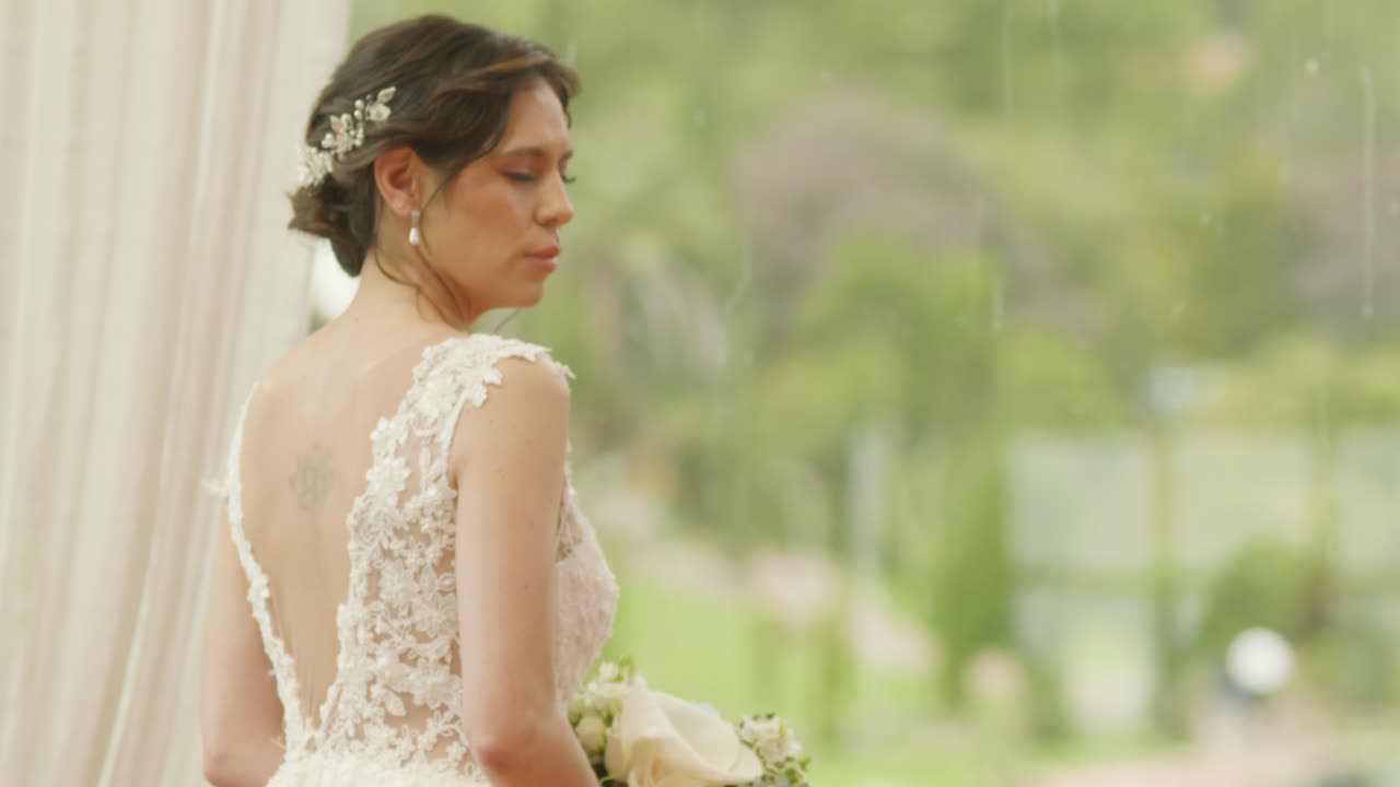 A bride, with her back turned, wearing a white dress, gazes at the horizon from a natural, rural setting. The rural setting highlights the purity and emotion of the moment.