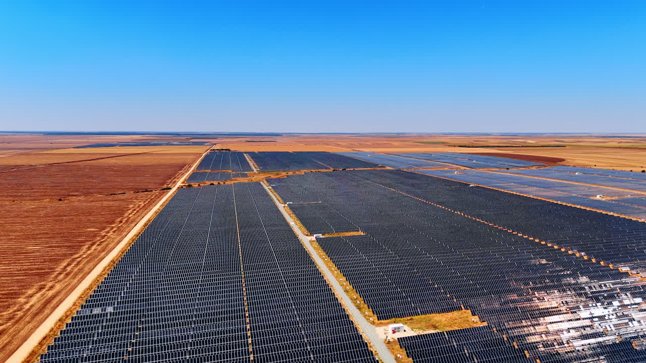 Large solar farm in sunny area. Rows of solar panels stretch across a flat landscape under a clear blue sky, emphasizing renewable energy efforts