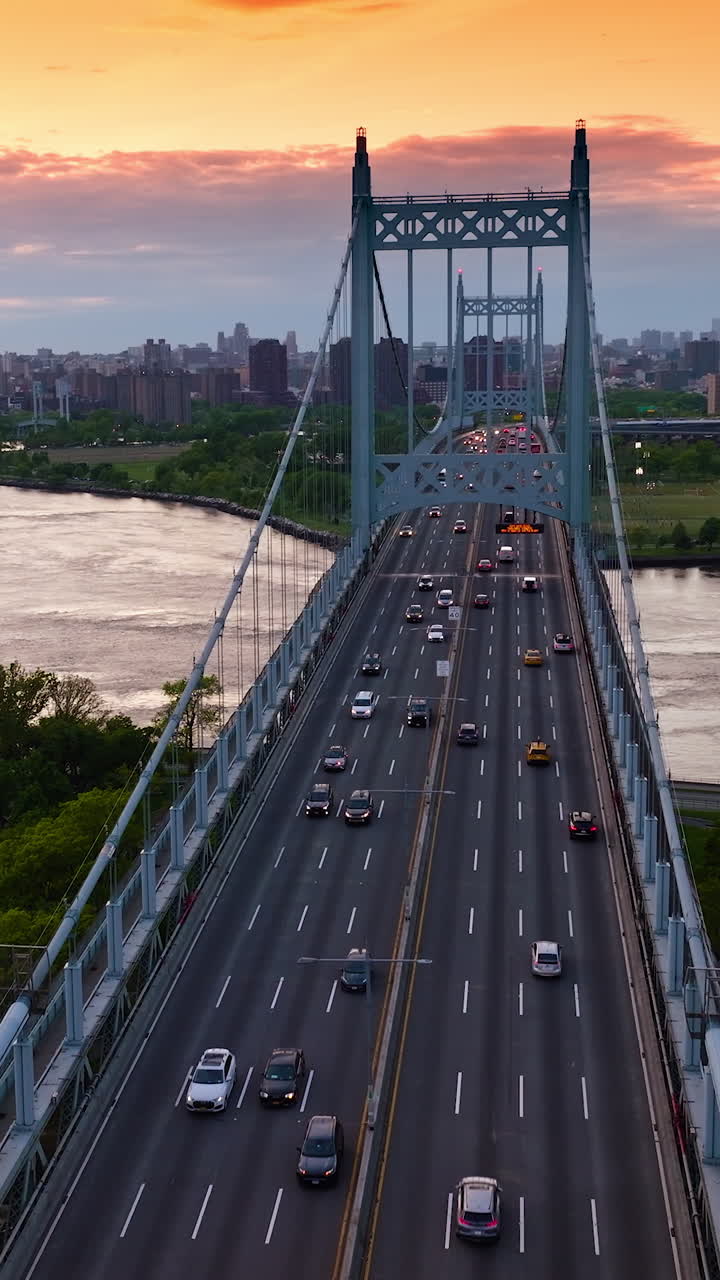Busy traffic on multi-lane roads of Robert F. Kennedy Bridge. Stadium and car park on both sides of bridge. Cityscape at backdrop. Vertical video