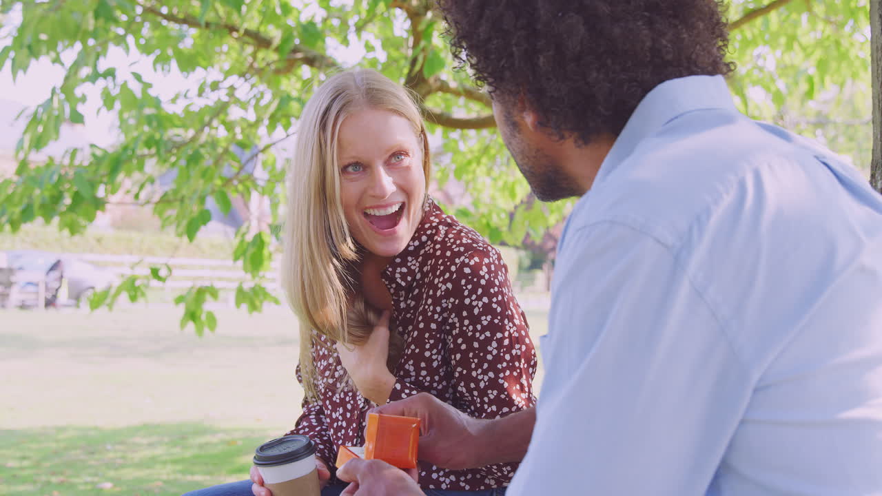un hombre maduro romántico le propone matrimonio a una mujer sorprendida sentada en un banco del parque con un anillo de compromiso en una caja.