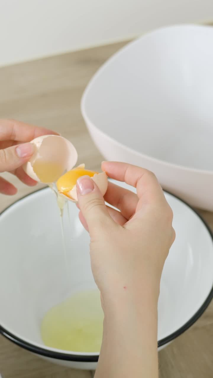 Vertical clip of cracking egg and separating yolk and white into separate bowls