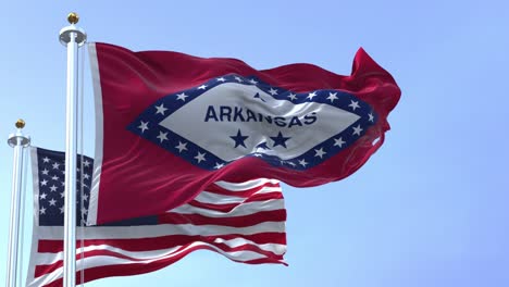 the flags of the arkansas state and united states waving in the wind.