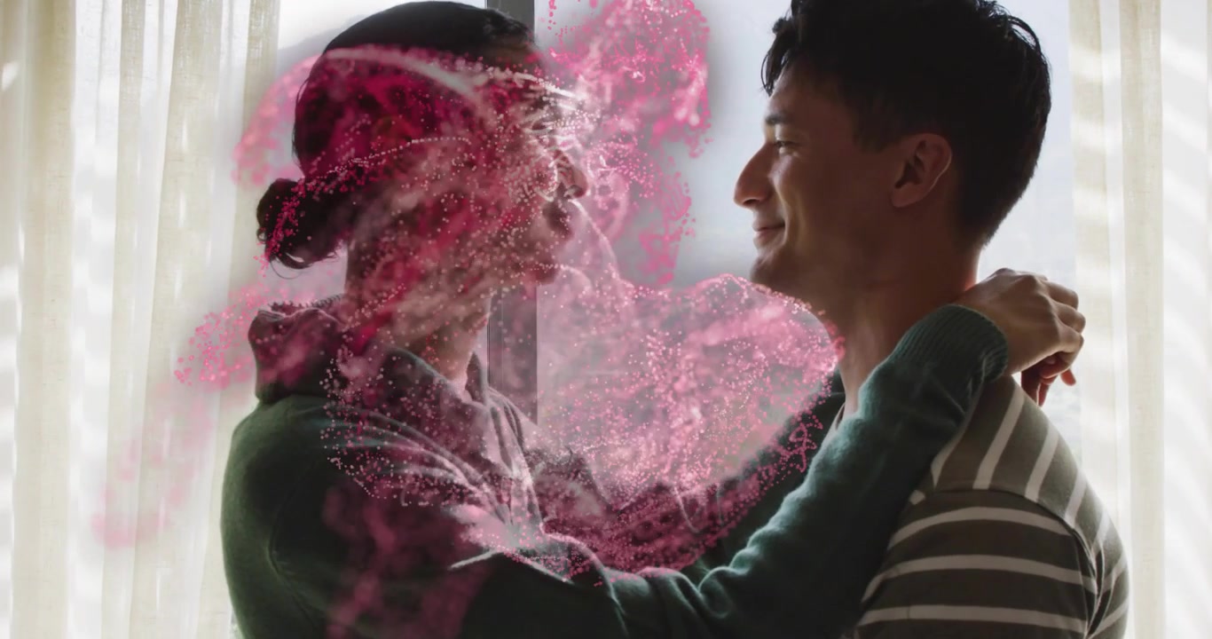 Coppia che si abbraccia accanto a una grande finestra, generando particelle rosa vorticose con effetti tecnologici che formano un alone.