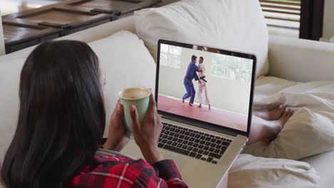 Composite-of-woman-sitting-at-home-holding-coffee-watching-judo-match-on-laptop