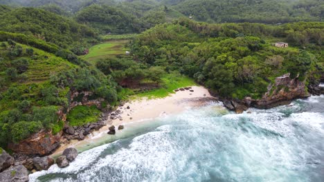 aerial top down shot of ocean waves reaching tropical private beach surrounded by deep rainforest in indonesia