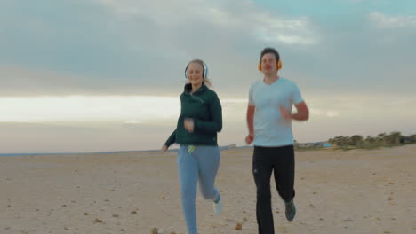 young couple in headphones running on the beach