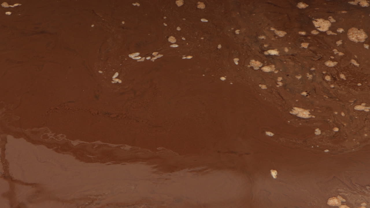 Concrete platform at a wastewater treatment plant pans down to reveal brown, swirling sewage water, highlighting industrial machinery and turbulent liquid motion